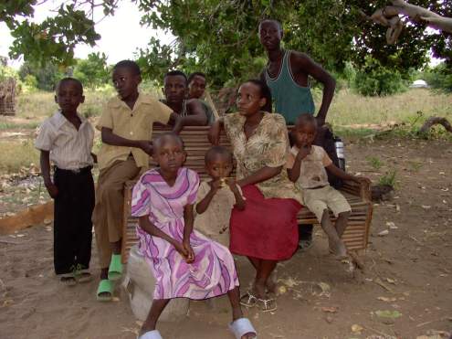 Im Vordergrund und rechts stehend eine Familie von Aidswaisenkindern, deren Eltern gestorben sind. Der 17j&auml;hrige junge Mann (rechts stehend) versorgt seine Geschwister inklusive seiner im Vordergrund sitzenden Schwester. Links hinten zwei zu Besuch gekommene Nachbarn.